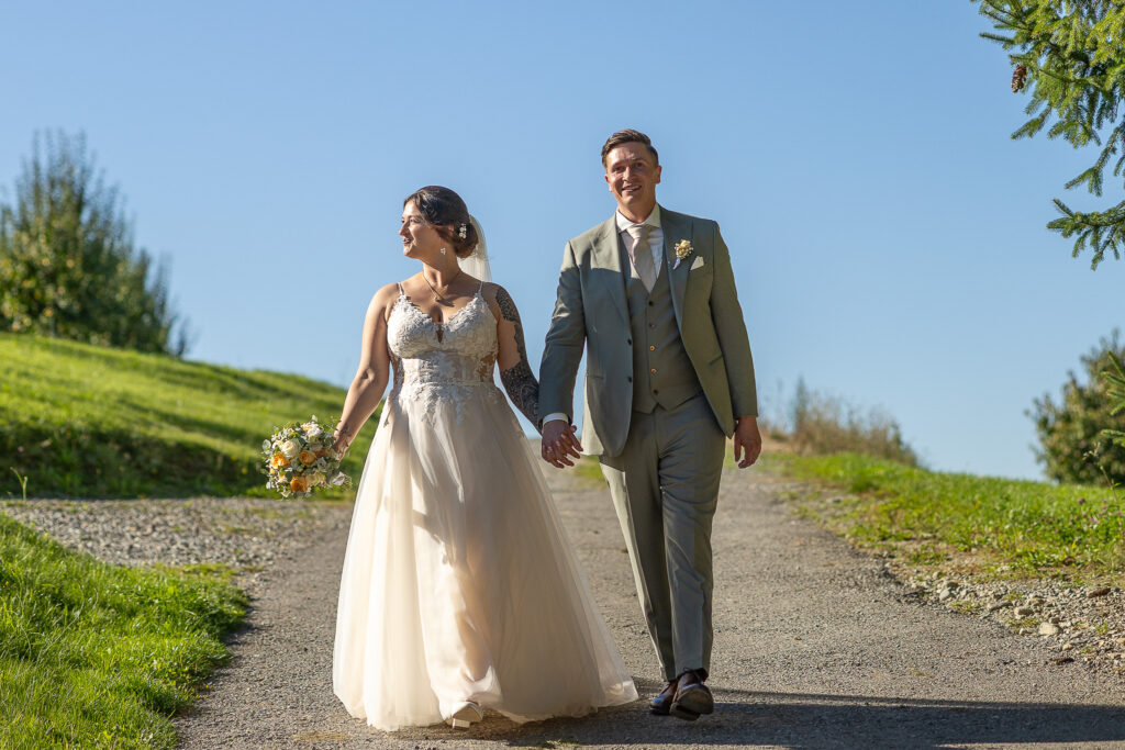 Brautpaar geht Hand in Hand auf dem Feldweg in der Abendsonne – Standesamtliche und kirchliche Trauung in Tettnang am Bodensee, Schloss Tettnang, Feier im Glashaus Tettnang