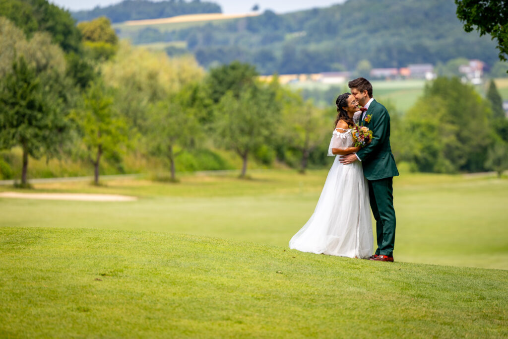 Brautpaar umarmt sich auf dem Fairway mit Blick auf die Hügel des Bodenseehinterlands – Deutsch-Mexikanische Hochzeit am Golfplatz Uhldingen-Mühlhofen, International Wedding